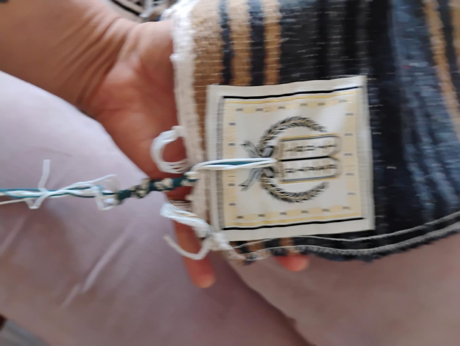 Corner plate embroidered with tablets inside a laurel wreath. Tzitzit, including a blue thread, pass through the plate.