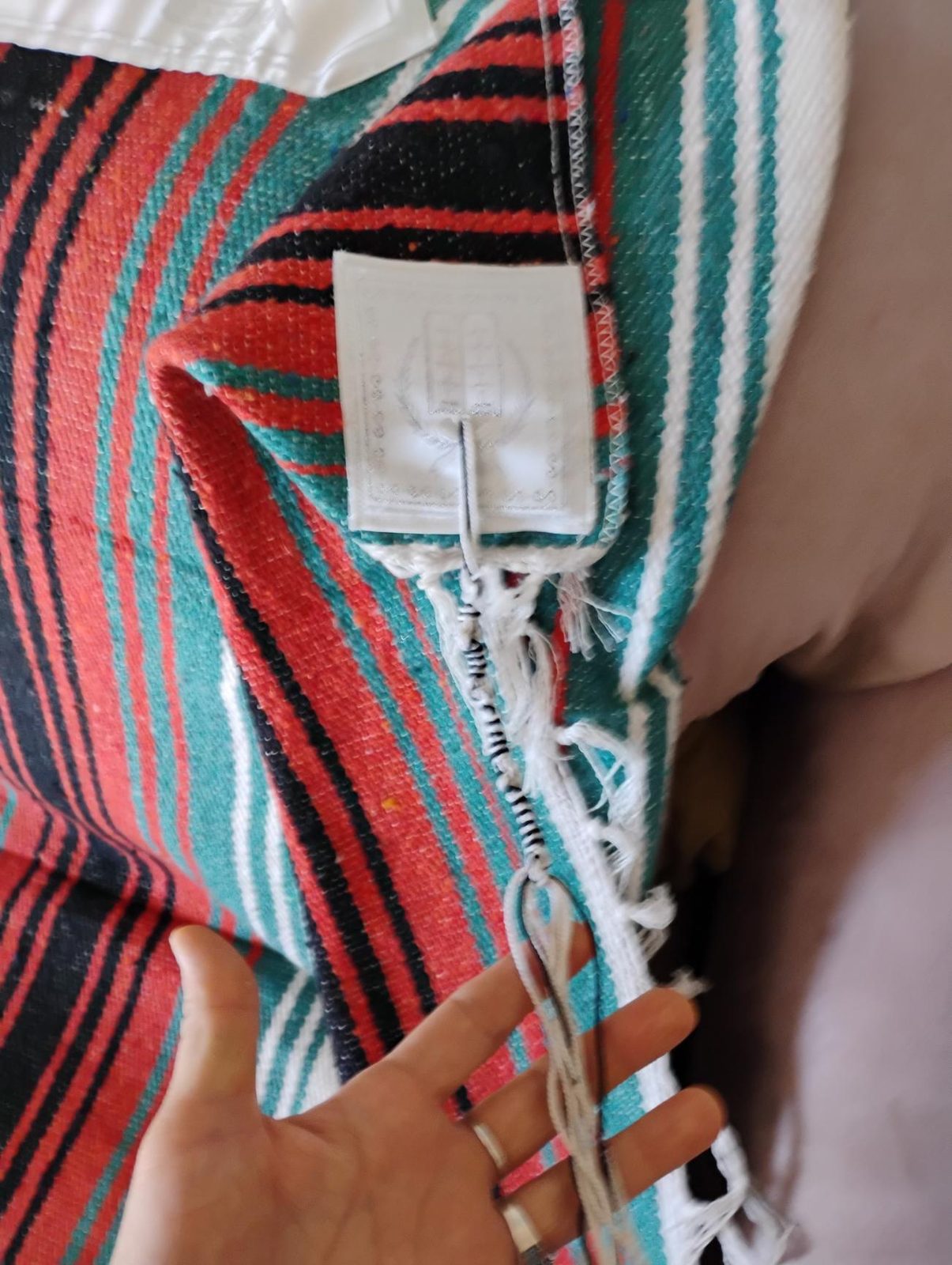 Tzitzit knotted and wound, held apart from the sarape’s own white hem fringe.